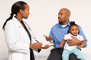 Father talking to doctor with baby on knee