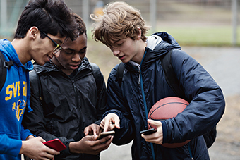 three teen boys looking at their phones with a basketball